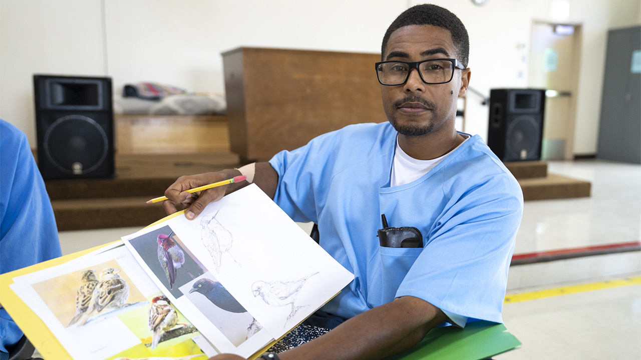 Man in blue scrubs holding a yellow photo album, looking at camera