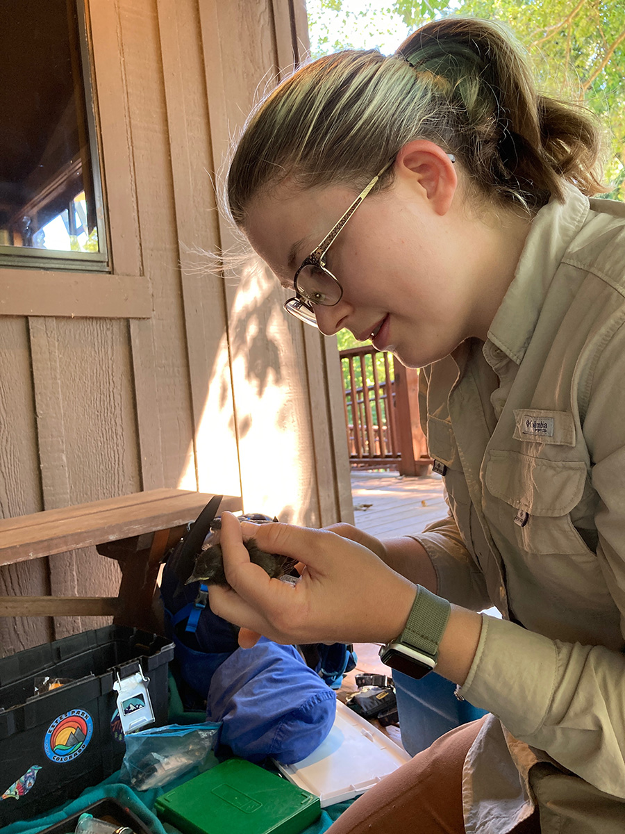 Young person in tan scout uniform at picnic table outdoors inspecting a small object