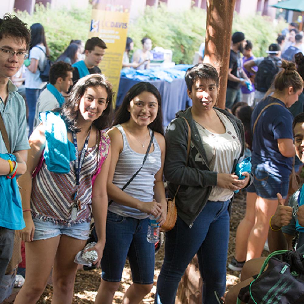 A group of students smiles at an outdoor UC Davis event, holding swag bags and water bottles.