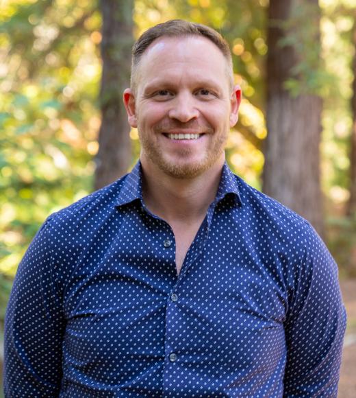 Smiling man in blue patterned shirt, casual portrait in sunlit forest