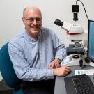 Dan Starr sitting in laboratory setting beside computer screen on which is an image of the roundworm.