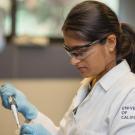 Female researcher in lab coat with goggles using a pipette