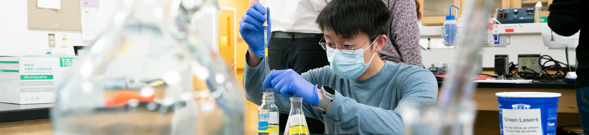 Male researcher with glasses and mask holding a beaker